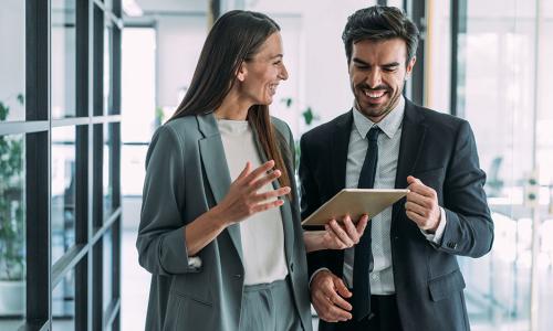 Two professionals walking in an office setting holding a tablet.