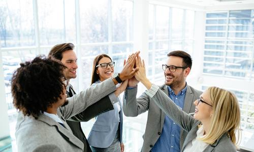Group of professionals high-five in an office setting.