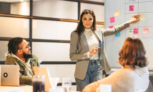Professional pointing at whiteboard in conference room.